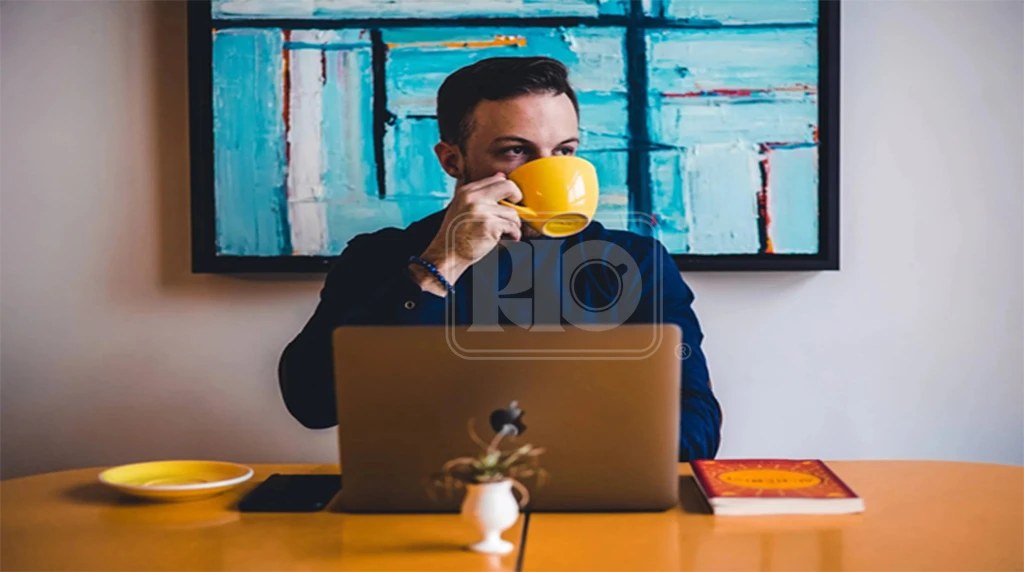 یک مرد پشت میز و مک بوک در حال نوشیدن قهوه